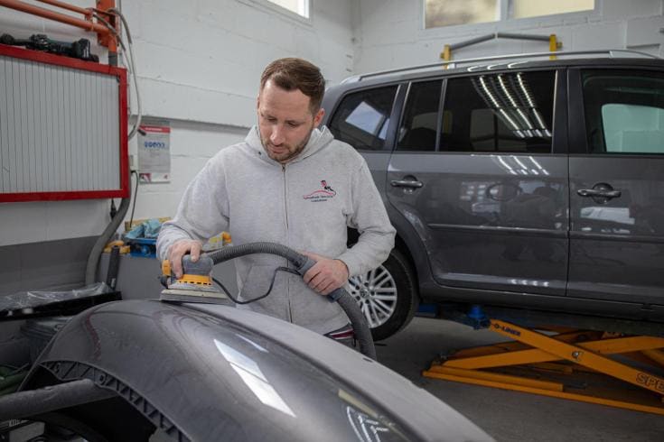 Schadehersteller schuurt een bumper met een excentrische schuurmachine